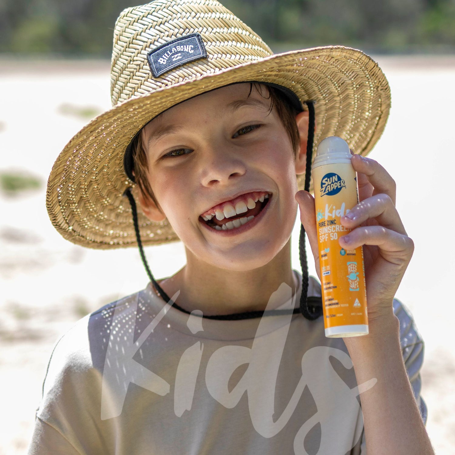 Child wearing a straw hat and holding a Sun Zipper Kids sunscreen bottle on a beach.