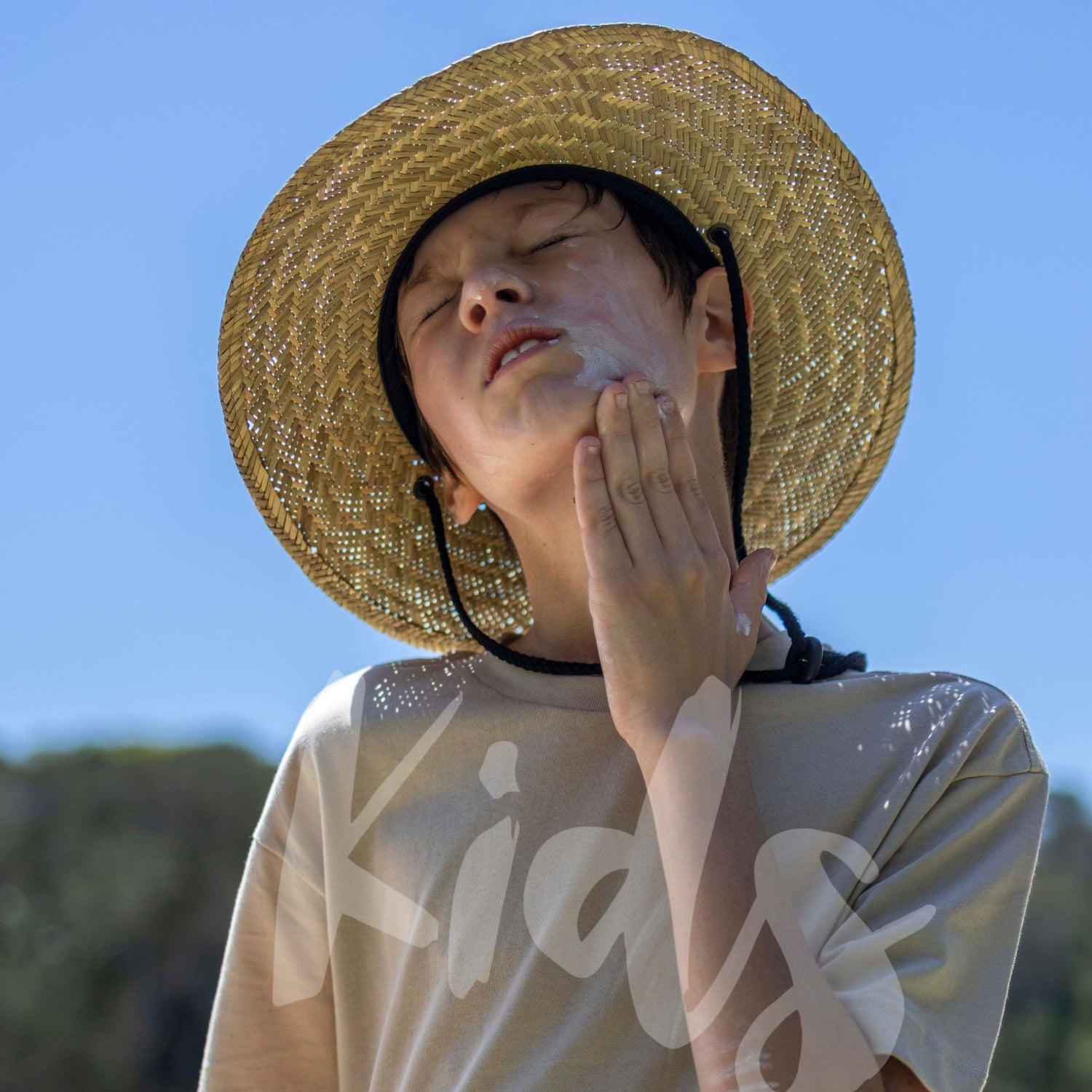 Person wearing a straw hat and a beige shirt with text, against a blue sky.