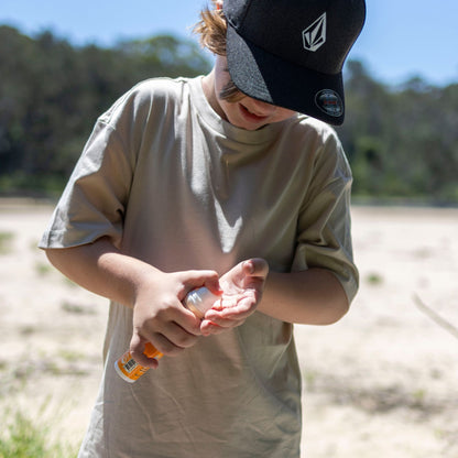 child outdoors applying kids mineral sunscreen to hands